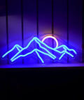 Sunrise Mountain Neon Light Sign USB Powered LED Wall Decor With Moon And Peaks glowing in blue and yellow on a shelf.