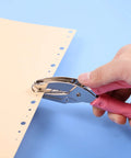 Hand using Three Piece Metal Handheld Hole Punch Set with pink plastic handle for DIY crafts on paper, showing hole creation for school supplies.