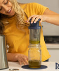 Woman using BPA-Free Reusable Oil And Butter Filter Press With Plunger And Brush, Mess-Free Infused Oil Strainer over a jar.
