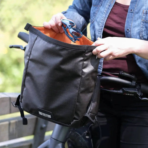 Person holding open Alpha Handlebar Bag 6 Liter for City Commutes and Bike Tours, Weatherproof Messenger With Roll Top And Tech Pocket