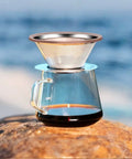 Stainless Steel Pour Over Coffee Dripper Cone 1 To 3 Cup on glass carafe by seashore, reusable metal filter, easy clean.