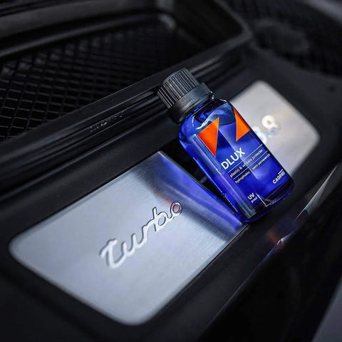 Blue CARPRO CQUARTZ DLUX wheel and trim coating bottle with black cap beside a silver Turbo badge.