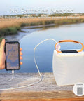 Two In One Solar Camping Lantern And Phone Charger for outdoor adventures with phone connected, near a scenic lake view.
