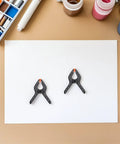 Must-Have 20-Ply Small Spring Clamps Kit For Woodworking And Photography Backdrop Clips Plus Heavy Duty Plastic Cloth Holders Perfect For Crafting, Home Improvement, Studio Work, Office Tasks, And Everyday Organization Adventures. Two small black plastic spring clamps on white paper
