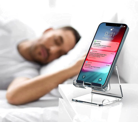 Crystal Clear Acrylic Phone Stand For Desk holding smartphone on nightstand next to sleeping man