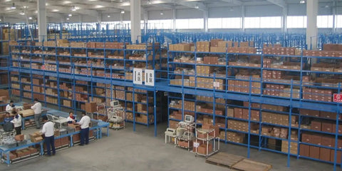 Large warehouse with shelves stacked with boxes and workers packing items in a clean, organized environment.