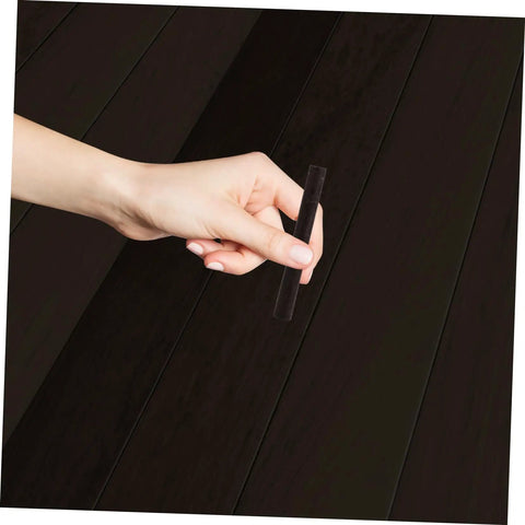 Hand holding 2 Pack Wood Filler Sticks for Furniture Repair Scratch Remover Pens Quick Fix Paint Markers against dark wood surface.