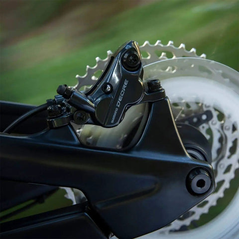 Close-up of Deore M6120 Hydraulic Disc Brake Front Post Mount Black Resin Pads Included Caliper on MTB wheel.