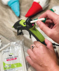 Inserting White Mini Fabric Hot Glue Sticks 4 Inch Length Machine Washable Adhesive into a glue gun, with crafts visible.