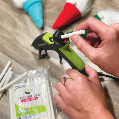 Inserting White Mini Fabric Hot Glue Sticks 4 Inch Length Machine Washable Adhesive into a glue gun, with crafts visible.