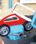 Vehicle Service And Repair Workbench Play Set With Realistic Tools For Young Builders Includes Drill Hammer Saw Wrench Tape Measure Bench Vice Gears Car Bodies Nuts And Bolts And Cardboard Garage Scene showing a saw cutting a toy car.
