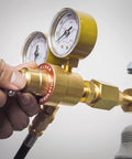 Close-up of brass welding gas regulator with dual gauges and attached hose on a cylinder.
