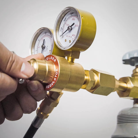 Close-up of brass welding gas regulator with dual gauges and attached hose on a cylinder.