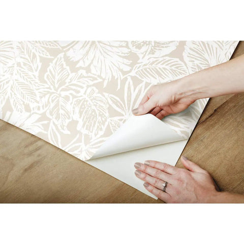 Hands applying Beige Batik Tropical Leaf Peel And Stick Wallpaper Roll 20 Point 5 Inches Wide By 16 Point 5 Feet Easy Drop Match Application