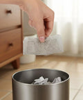 Hand holding Ten Pack Square Disposable Shower Drain Hair Catcher Stickers above a trash can for easy disposal.