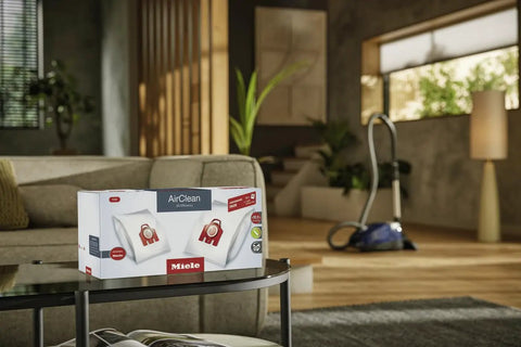 HyClean Air FJM Vacuum Bags For Compact C1 And C2 Canisters box on table in living room with vacuum cleaner in background