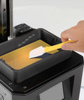 Hand using a silicone spatula from the Must-Have 7-Piece UV Resin 3D Printer Cleaning Kit With Silicone Spatulas, Scrapers, And Brushes For Resin Transfer