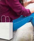 Medium White Kraft Paper Bags With Handles 8x4.75x10 Inches Bulk Pack Of 100 sitting beside person on steps