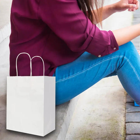 Medium White Kraft Paper Bags With Handles 8x4.75x10 Inches Bulk Pack Of 100 sitting beside person on steps