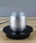 Fast Acting USB Mug Warmer With Smart Adjustable Heat Control Keeps Your Morning Sip Piping Hot All Day Long Sleek Black Tempered Glass Platform with a silver mug.