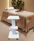 Premium Iron Wood Aluminum Salon Trolley With Smooth Rubber Wheels Built Tough Rolling Beauty Station Cart For Hair Stylist Tool Storage And Salon Floor Organization Game Changer in a spa setting with a cream quilted bed.