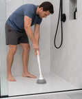 Man using a Slick Modern Toilet Plunger With 19 Inch Handle And Gray Rubber Cup in a shower to clear clogs.