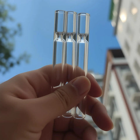 Close-up view of hand holding three 4-inch borosilicate glass tubes against a blue sky, part of Six Pack Borosilicate Glass Tubes For Lab And DIY Blowing, 4 Inch Length, 12 Mm Outer Diameter, 2 Mm Thick Wall, High Heat And Chemical Resistant, Premium Glass Tubes For Science Projects, Glassblowing And Crafting.
