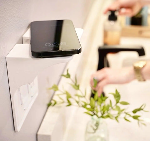 White double wall outlet shelf with cord storage strap, holding a phone, installed in bathroom, showing space-saving design.