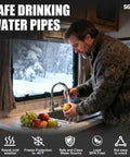 Blue SGNJT heated RV drinking water hose; man at camper kitchen sink washing an apple, snowy window outside.