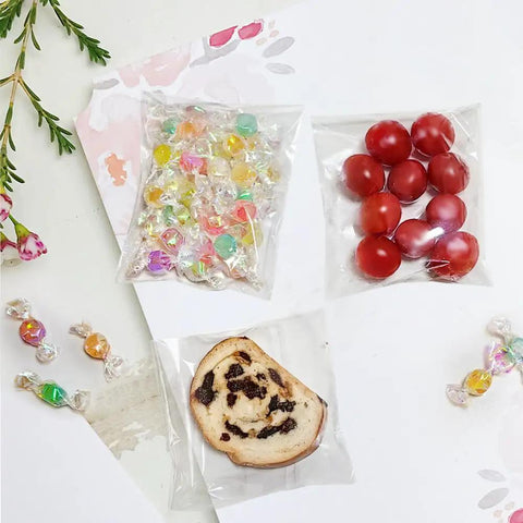 Clear 4x4 Inch Resealable Cookie Bags, 200 Pack, Self Sealing Cellophane Bags For Cookies, Candy, Treats, Favors, Jewelry, And Gift Wrapping, Thick 2.8 Mil For Premium Packaging displaying colorful candy, tomatoes, and a cookie.