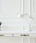 White desk with Vintage Bronze Patina Finish Cabinet Hardware Set floral pulls, lamp, and plant, in bright room with paneled wall.