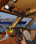 Boat dashboard with heavy duty handheld radio holder for walkie talkie and speaker mic mounted, view of cargo ship outside window.