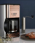 Rose Gold Drip Coffee Maker For Home Office And Small Kitchen With One And A Half Liter Water Tank 910W Power One Button Operation Anti Drip Timed Temperature Control Fine Filter Durable PP Material Compact shown on a kitchen counter next to baked goods.
