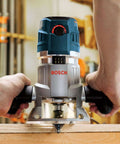 Bosch router in blue and silver, held by hands while routing a wooden board.