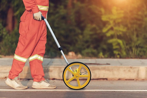 Person walking with a Heavy Duty Measuring Wheel With Foldable Handle And Mechanical Counter for outdoor surveying.