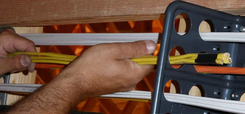Hands using Box Of Fifty H2 Homer Helpers For Electrical Wire Management to organize yellow cables in a rugged bracket.