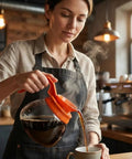 Woman pouring coffee from 64 Oz Commercial Glass Coffee Pot Decanter With Orange Decaf Handle at cafe counter