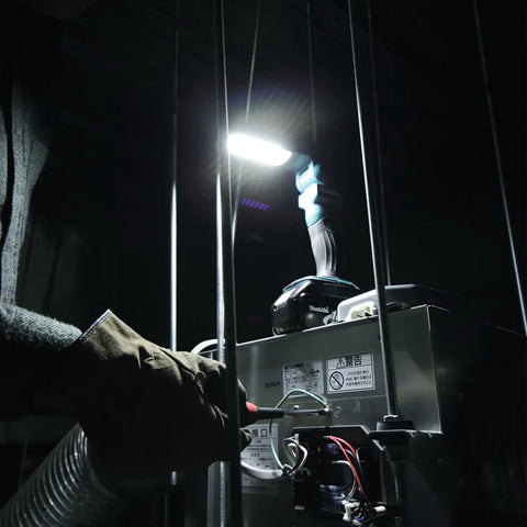 Worker using 18V LXT Cordless 12 LED Flashlight With Foldable Head And 360-Degree Swivel Hook in dark worksite, detail view.