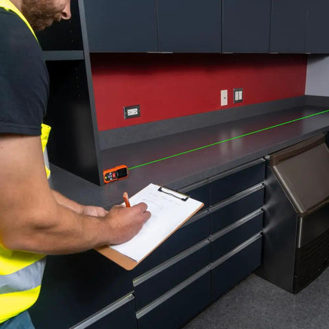 Man using Green Laser Distance Measure Tool with 200 foot range on countertop, USB rechargeable, class 2 laser visible.