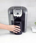 Person using Patented Iced Coffee And Beverage Cooler That Chills In One Minute, 12.5 Oz, Black with coffee machine.