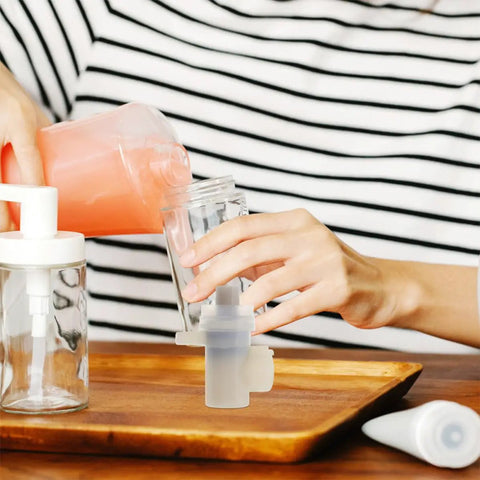 Person pouring liquid into a glass jar while using a Slick Replacement Soap Pump Head for Liquid Soap and Lotion Dispensers.