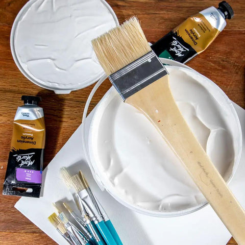 Premium Gesso Universal Primer 64oz with brushes and paint tubes on wooden surface