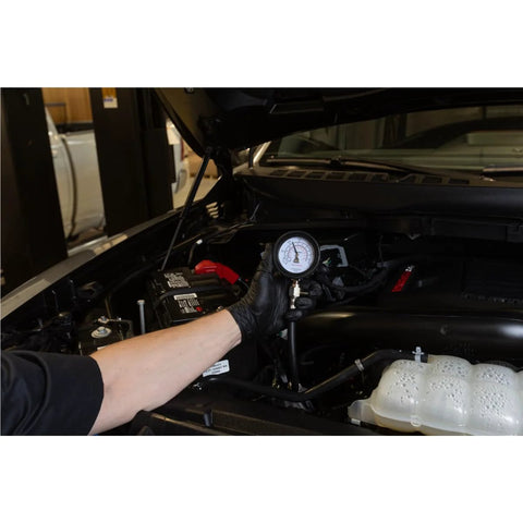 Mityvac engine compression test gauge held by black-gloved hand under car hood