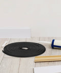 Heavy Duty Rubber Caulk Saver Strip For Concrete Joints Built Nails Tough Hella Flexible Black Weatherproof Wall Door Gap Sealer Universal Crack Stopper Five Meter Roll coiled on wooden floor with caulk gun.