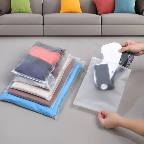 30 Pack Transparent Reusable Clothes Storage Bags With Zip Lock For Travel And Storage Grab And Go Durable Frosted Waterproof Organizers being used to pack clothes and accessories on a floor.