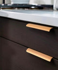Close-up of gold invisible flush pull handles on dark cabinet doors in a kitchen setting.