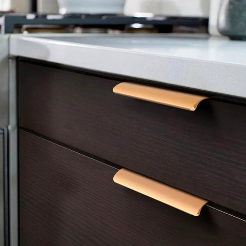 Close-up of gold invisible flush pull handles on dark cabinet doors in a kitchen setting.
