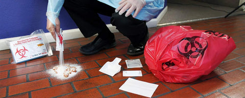 22-piece bodily fluid cleanup spill kit with red biohazard bag on tiled floor.