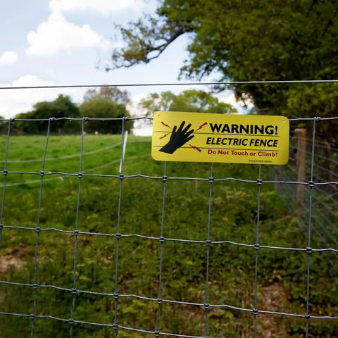 Four Pack Electric Fence Warning Signs Heavy Duty High Density Plastic Rock Solid Outdoor Yard Perimeter Security Panels Weather Resistant 10 By 3 5 Inches, visible on fence, indicating danger of electric shock.