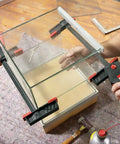 No Sweat One Hand Clamp And Spreader For Tough Woodworking in use, securing glass panels with balanced lever grip.